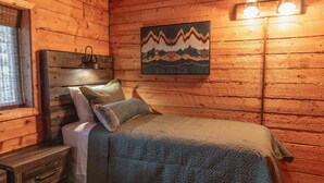 A wooden cabin bedroom with a bed, nightstand, and wall-mounted light fixture. - Technology Free & Dogs are Welcome (Lake City)