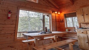 A wooden cabin interior with a large dining table, benches, and a kitchen area. - Technology Free & Dogs are Welcome (Lake City)