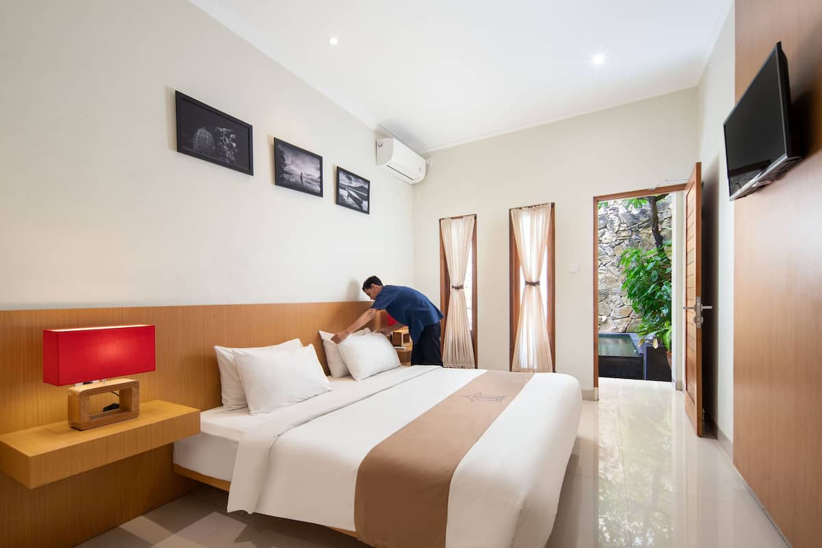 Une chambre d’hôtel avec un lit, une table de chevet surmontée d’une lampe rouge, un téléviseur à écran plat fixé au mur et une fenêtre avec des rideaux.