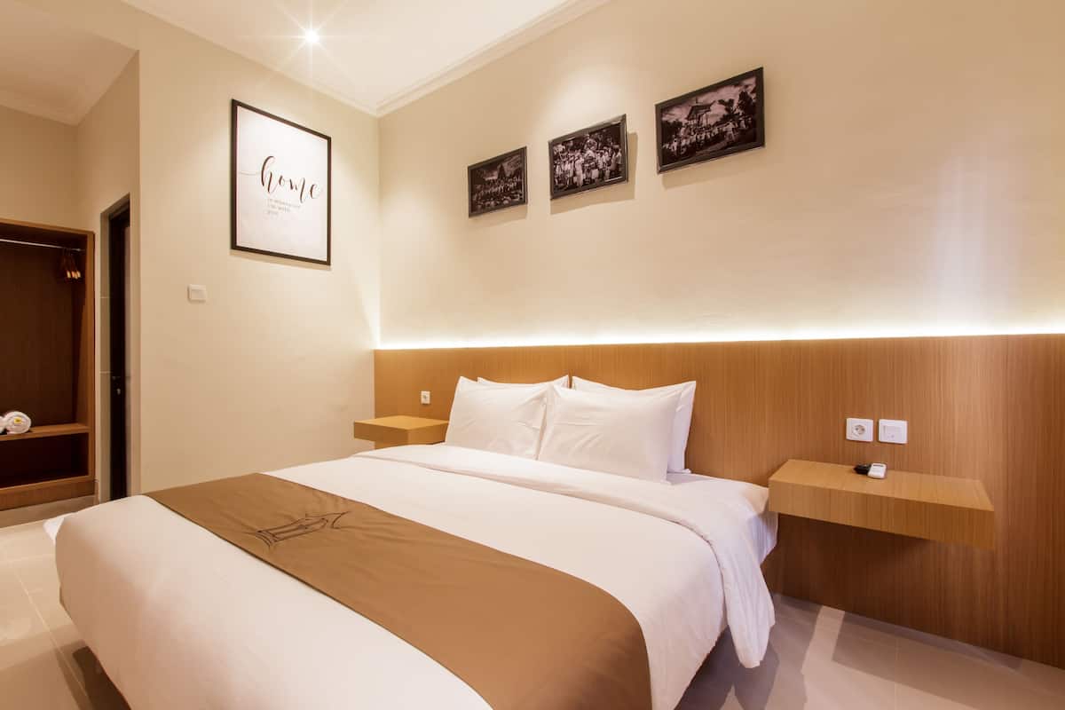 Une chambre d’hôtel avec un grand lit, une tête de lit en bois, des tables de chevet, une étagère avec un téléphone et des tableaux encadrés au mur.