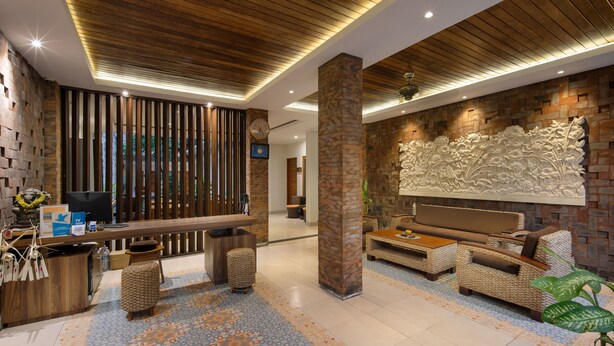 A reception area with a wooden reception desk, seating area with sofas, and a decorative wall. - Angkul Angkul Segara Beach Kuta (Kuta)