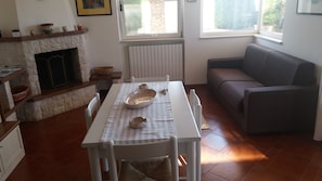 Et spiseområde med pejs, et bord dækket med skåle og en sofa i et rum med et vindue.