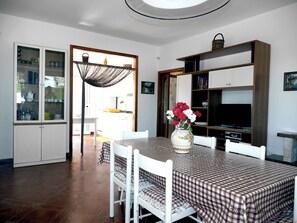 A dining area with a checkered tablecloth, white chairs, a vase with flowers, and a kitchen in the background. - Villa GenVi - Private Villa with a Saltwater Pool (Polignano a Mare)