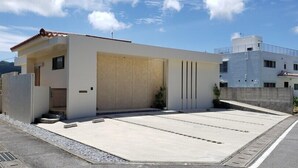 A modern two-story house with a flat roof, a large garage door, and a paved driveway. - Chakashiya Goten (Onna)