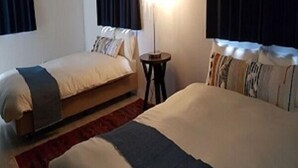 A hotel room with two beds, a nightstand, and a lamp. - Chakashiya Goten (Onna)
