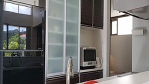 A modern kitchen with a built-in refrigerator, a microwave, and a window with a view of greenery. - Chakashiya Goten (Onna)