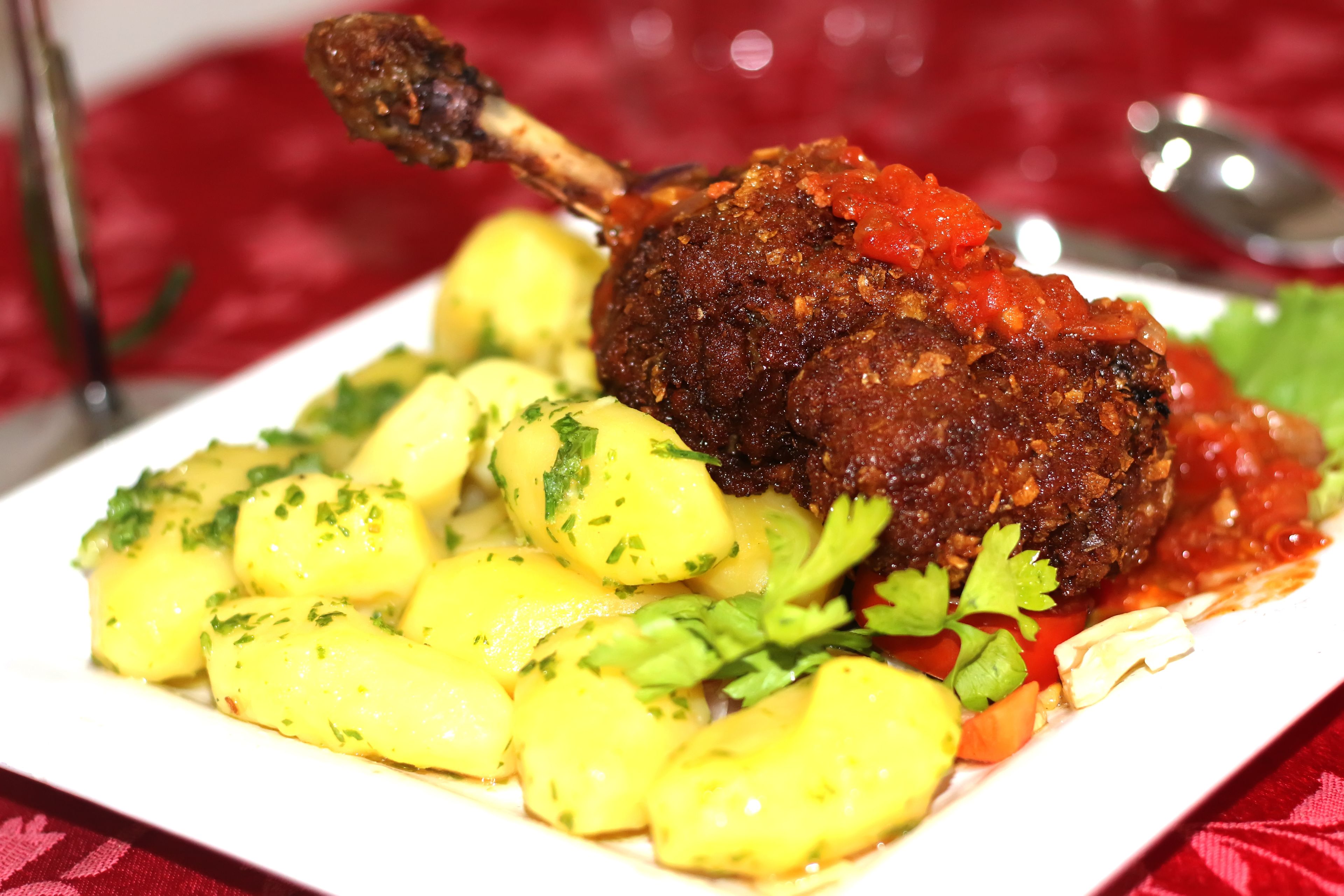 Ein Teller mit gebratenem Lammkeule, Salzkartoffeln und Tomatensauce.