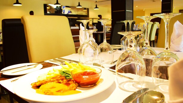 A dining table set with plates, cutlery, and wine glasses in a restaurant. - Crystal Palace Hotel (Abuja)