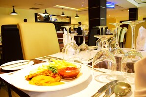 A dining table set with plates, cutlery, and wine glasses in a restaurant. - Crystal Palace Hotel (Abuja)
