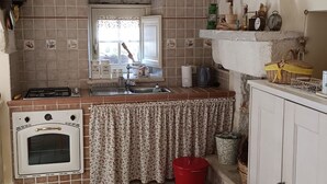 A rustic kitchen with a stone ceiling, a window with floral curtains, a stove, an oven, and a sink.