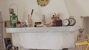 A rustic kitchen with a stone wall, a shelf with kitchen utensils, a red pot, and a wicker basket.