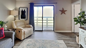 A living room with a beige sofa, a gray sofa, a patterned rug, a starfish decoration, and a sliding glass door with blue curtains. - Coastal Oasis w/ Amazing Views Just Steps From The Sand + Pool Access (Tybee Island)