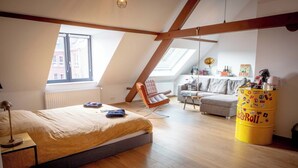 Une chambre à coucher aménagée dans un espace mansardé, avec un plafond en pente, un lit, une chaise, un canapé et un tonneau jaune.