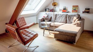 Une pièce de style « loft », avec un plafond haut, une lucarne, un fauteuil en cuir, un canapé gris et une petite table ronde.
