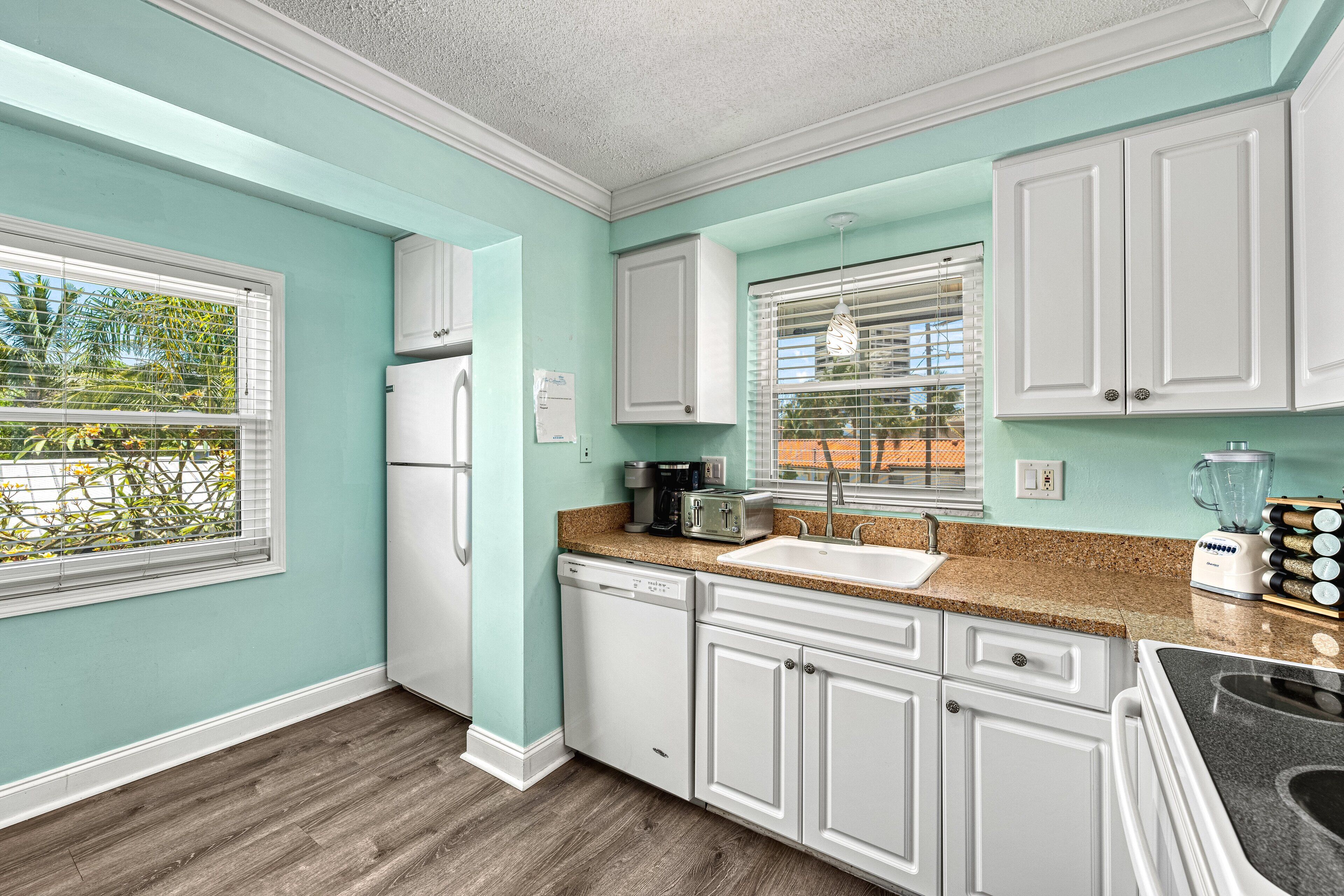 A kitchen with white cabinets, a dishwasher, a refrigerator, a sink, and a granite countertop.