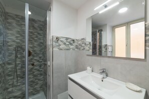 A modern bathroom with a glass-enclosed shower, a white sink with a mirror above it, and patterned tiles on the walls.