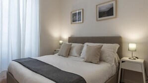 A neatly made bed with a grey throw blanket, two bedside lamps, and two framed pictures on the wall. - Modern, cozy and comfortable by Fontana di Trevi (Roma)