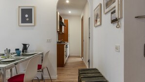 A narrow hallway with a dining area on one side, featuring a table set with plates, cups, and a pitcher. There are framed pictures on the walls and a staircase leading to another level. - Modern, cozy and comfortable by Fontana di Trevi (Roma)
