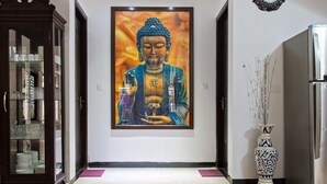 En hall med en stor målning av Buddha, ett skåp med glasföremål och en dekorativ vas.