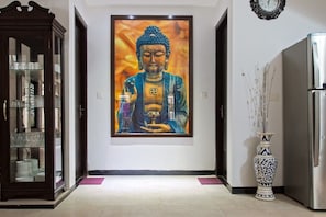 A serene hallway features a striking Buddha painting, a display cabinet, and a tall vase, set against a backdrop of a beautifully tiled floor.