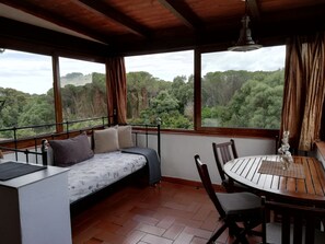 Ein gemütliches Zimmer mit Bett, Tisch und Stühlen, große Fenster mit Blick auf ein bewaldetes Gebiet.