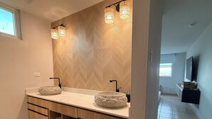 A modern bathroom with a double sink, wooden cabinetry, a large mirror, and a herringbone-patterned wall.