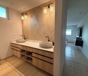 A modern bathroom with a double sink, wooden cabinetry, a large mirror, and a herringbone-patterned wall.