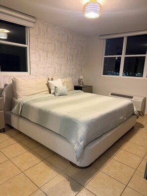 A bedroom with a bed, nightstand, lamp, window, and radiator.