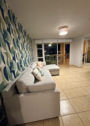 A living room with a sectional sofa, a patterned wall, and a view of the outside.