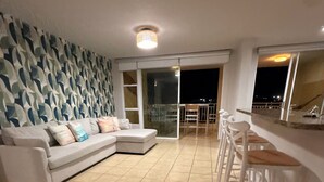 A living room with a sofa, a patterned wall, a balcony with a railing, and a bar area.