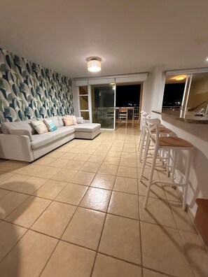 A living room with a sofa, a patterned wall, a balcony with a railing, and a bar area.
