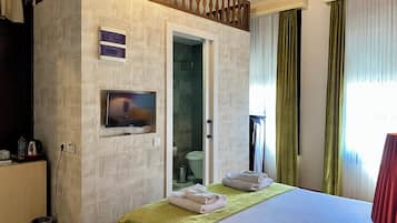 Habitació d'hotel amb un llit, una televisió penjada a la paret, un petit armari i una porta que dona a un bany.