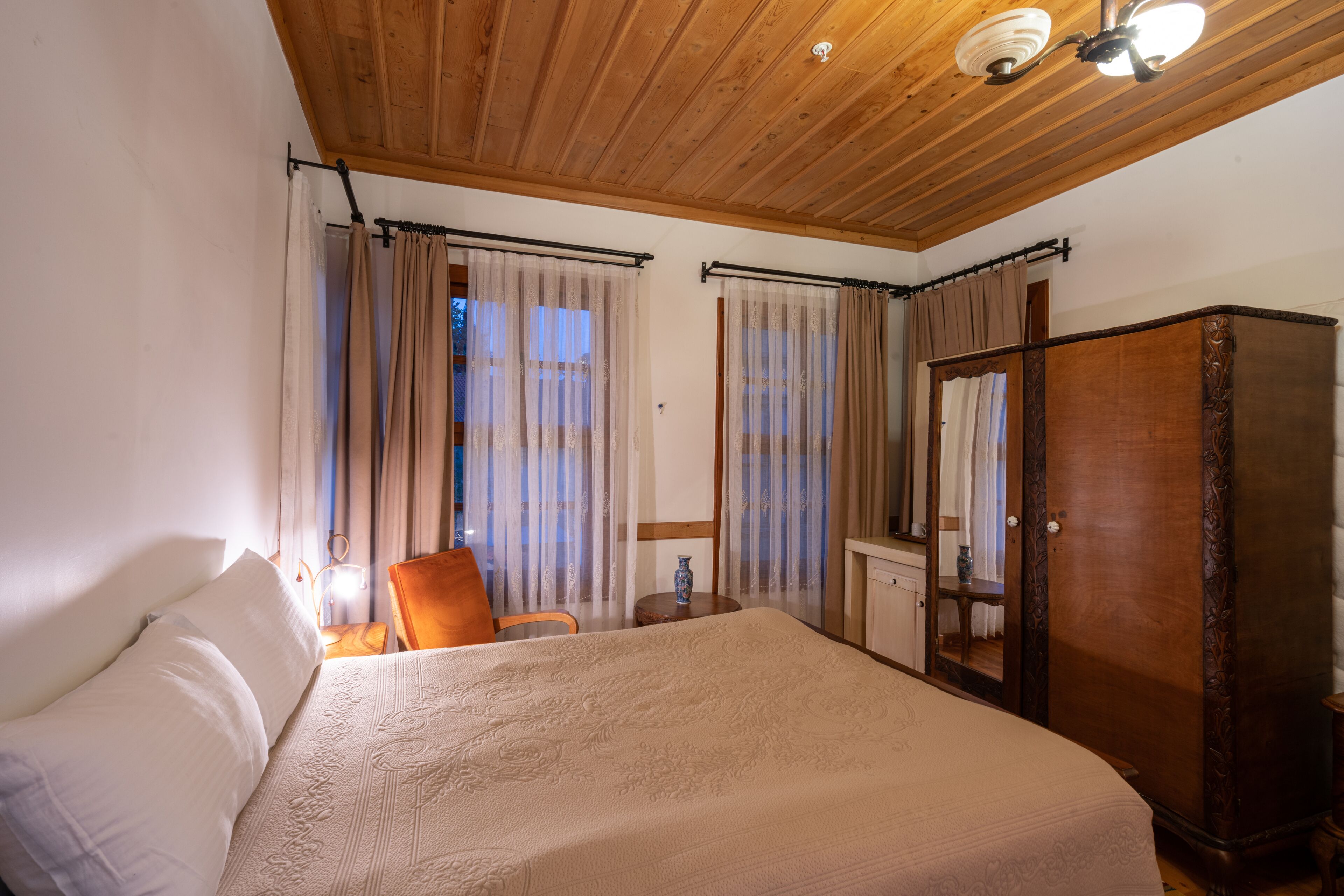 A bedroom with a large bed, wooden ceiling, and curtains.