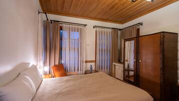 A bedroom with a large bed, wooden ceiling, and curtains.