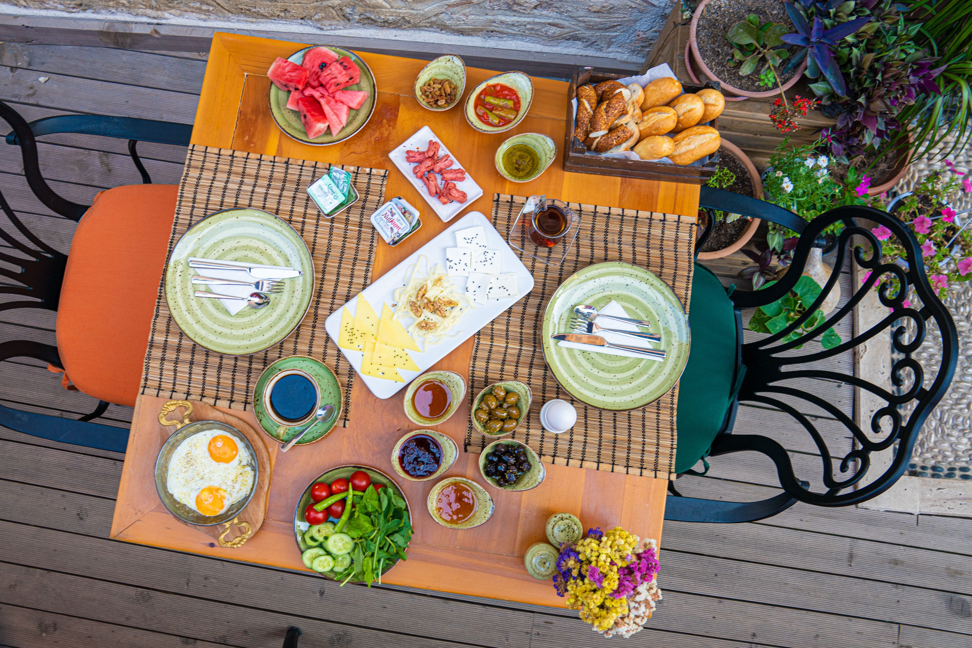 A table set with various dishes, including eggs, salads, and bread, surrounded by chairs and potted plants.