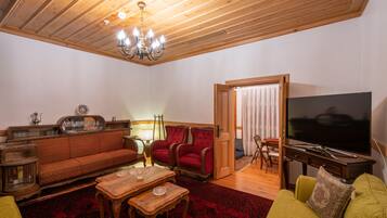 Una sala de estar acogedora con techo de madera, un sofá rojo, un sillón verde, una mesa de centro de madera y un televisor de pantalla plana.