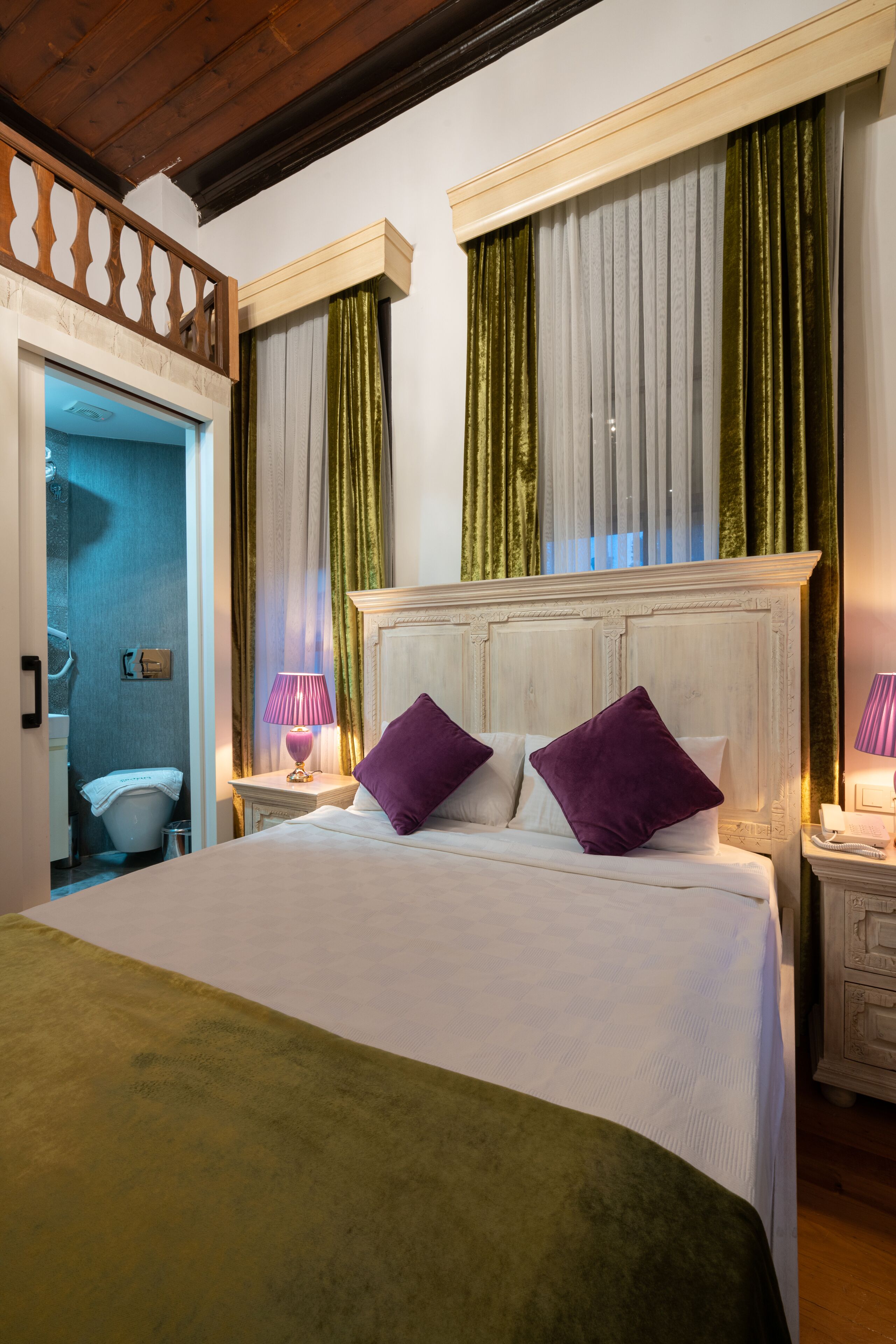 Ein Hotelzimmer mit einem großen Bett, zwei Nachttischen, einem Holz-Kopfteil und einem durchgehenden Türbogen einsehbaren Badezimmer.