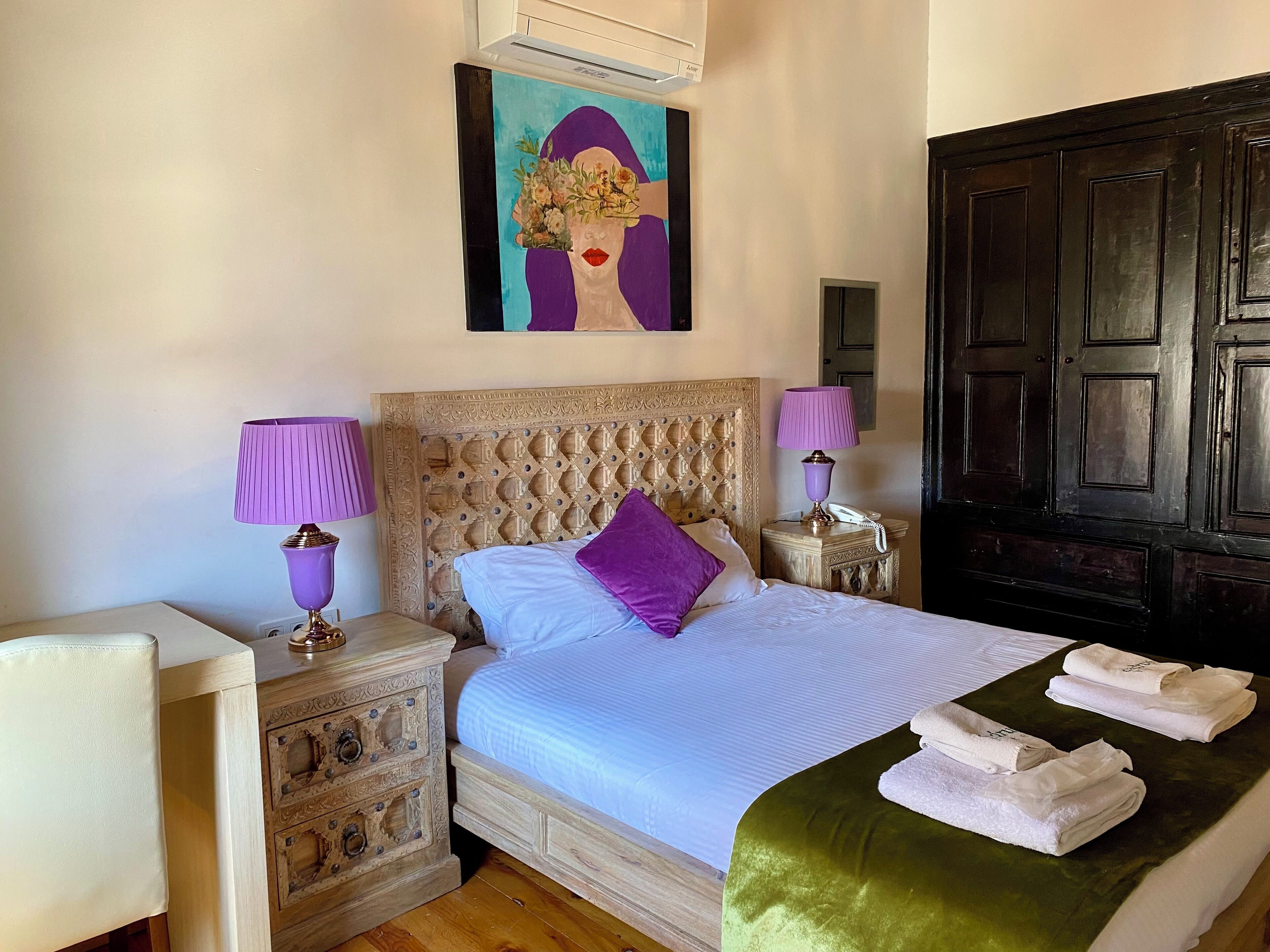 A neatly arranged bedroom with a large bed, two bedside lamps, a wooden nightstand, and a decorative headboard.