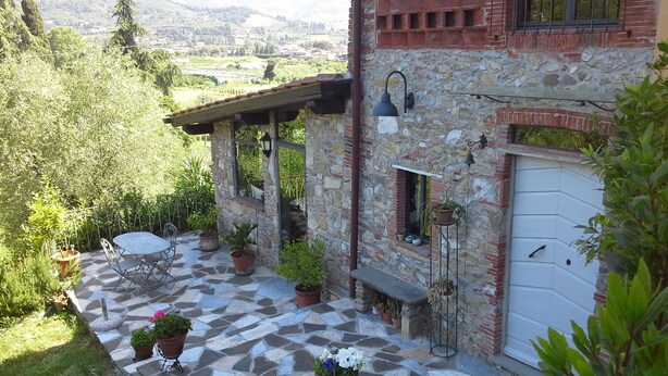 Un bâtiment en pierre doté d’un patio comprenant une table et des chaises, des plantes en pot et une vue sur la campagne.