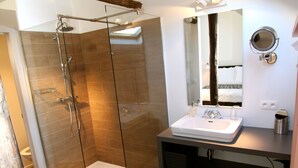 Ein modernes Badezimmer mit einer gläsernen Duschkabine, einem weißen Waschbecken und einem großen Spiegel.