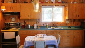 A wooden cabin kitchen with a dining table, chairs, and a window. - Enjoy Sunset views on tranquil Dexter Pond (Winthrop)