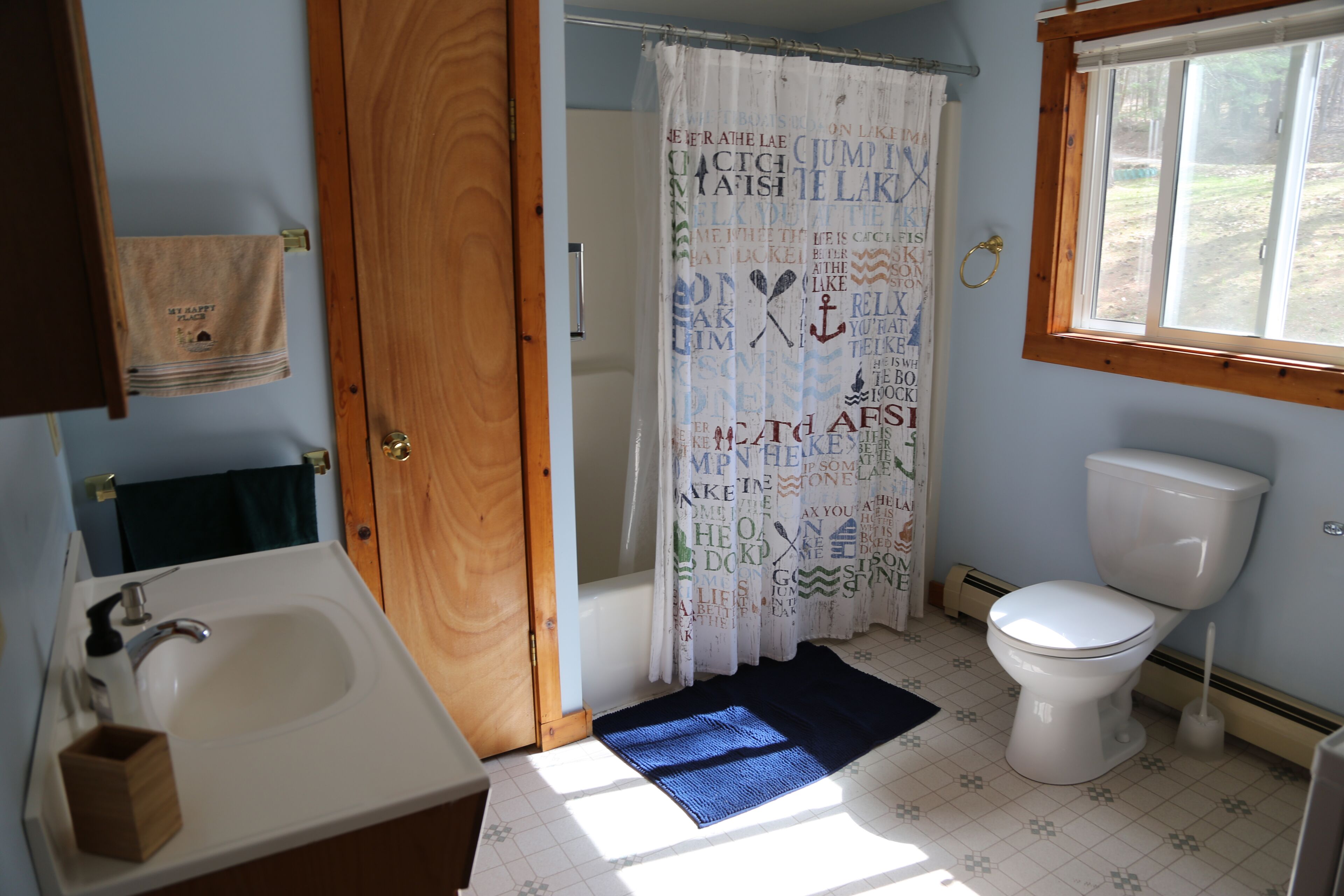 Ein Badezimmer mit Holztür, Waschbecken in Weiß, Toilette und Duschvorhang mit Text.