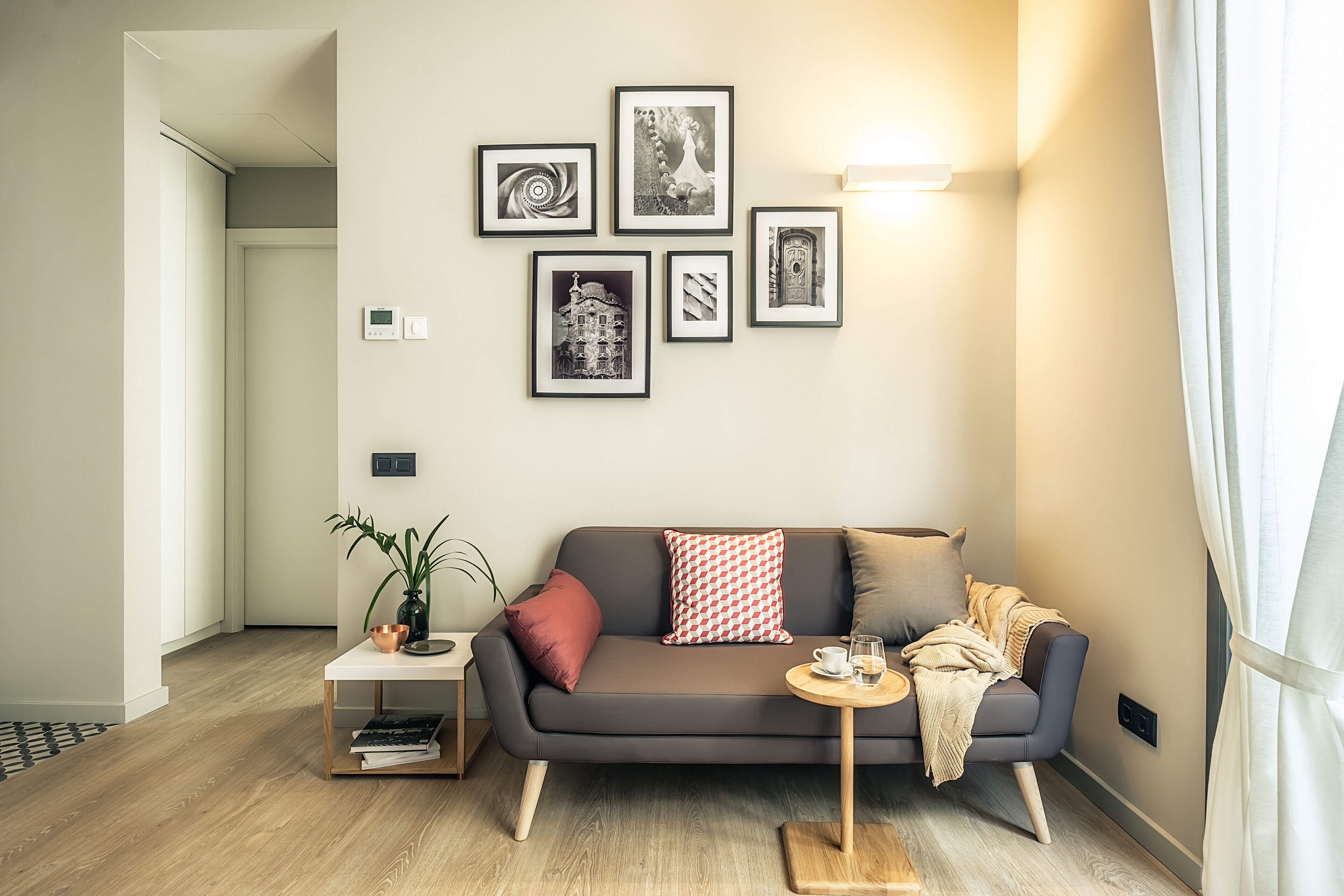 Een moderne woonkamer met een grijze bank, een klein rond tafeltje en een plant in een pot.