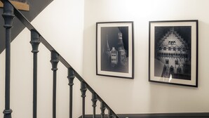 A staircase with black balusters and wooden steps, leading to a landing with two framed black-and-white photographs on the wall.