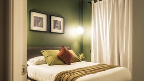 A neatly made bed with a white comforter and a brown throw blanket, a green wall, and two framed pictures above the bed.