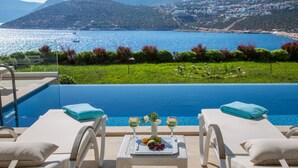 A poolside view with two lounge chairs, a table with a fruit platter, and a view of the sea and hills. - Villa Setara is a rare beach front property located in Kalkan (Kalkan)