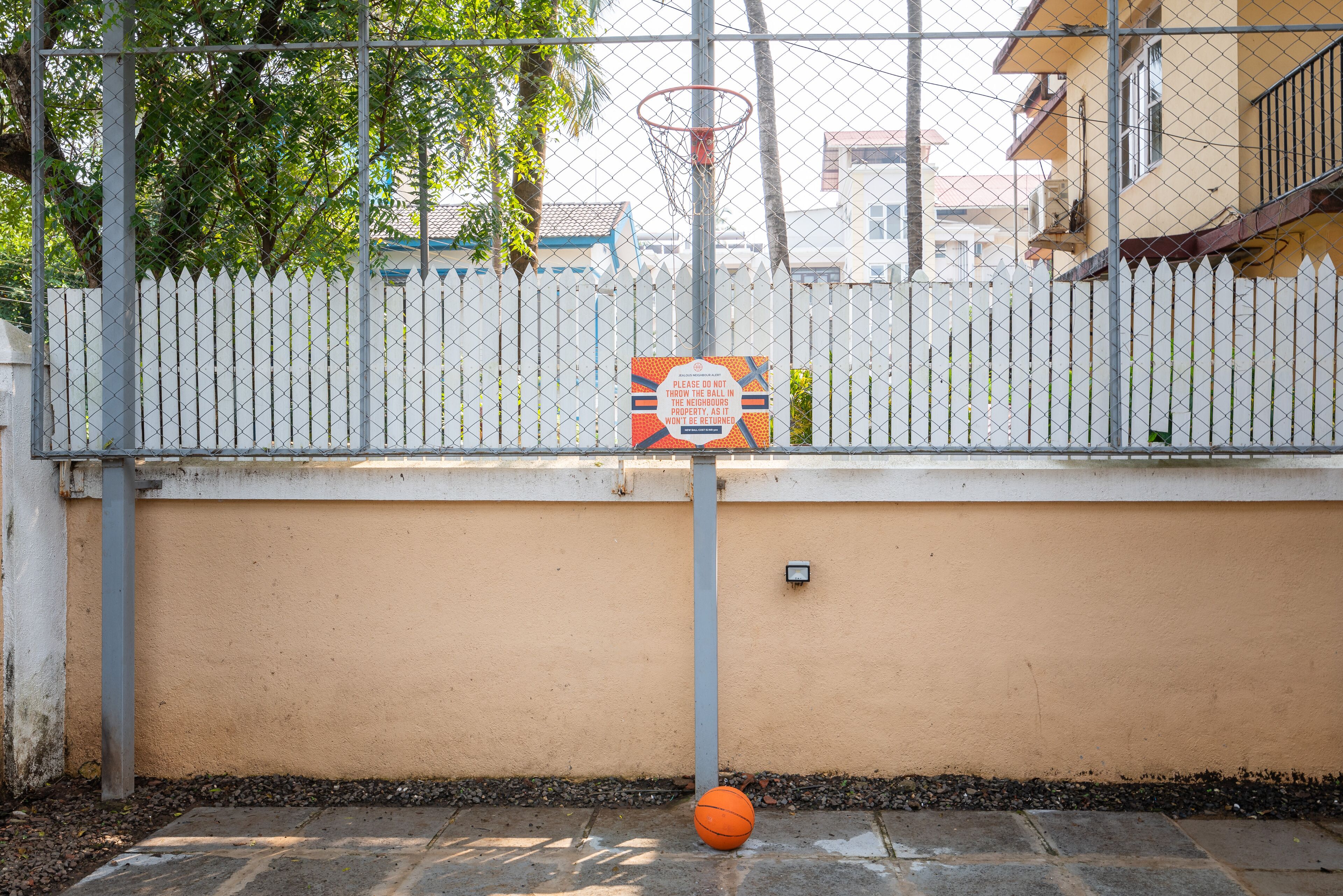 A basketball hoop with a sign, a white picket fence, and a building in the background.