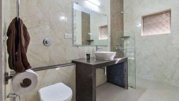 A modern bathroom with a marble wall, a glass shower enclosure, a white sink, and a toilet. - 6 bedroom Private Villa on Adventure Street with Large Garden and Pool Table (Calangute)
