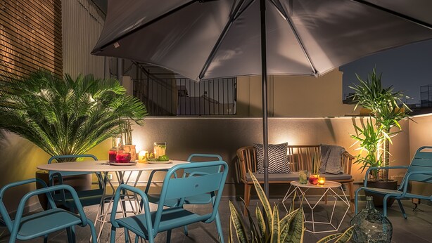 Un'area patio all'aperto con tavolo e sedie, un ombrellone grande e piante in vaso.