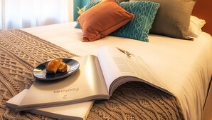 Un letto rifatto con una coperta a motivi, un libro e un piatto di cibo su un comodino.